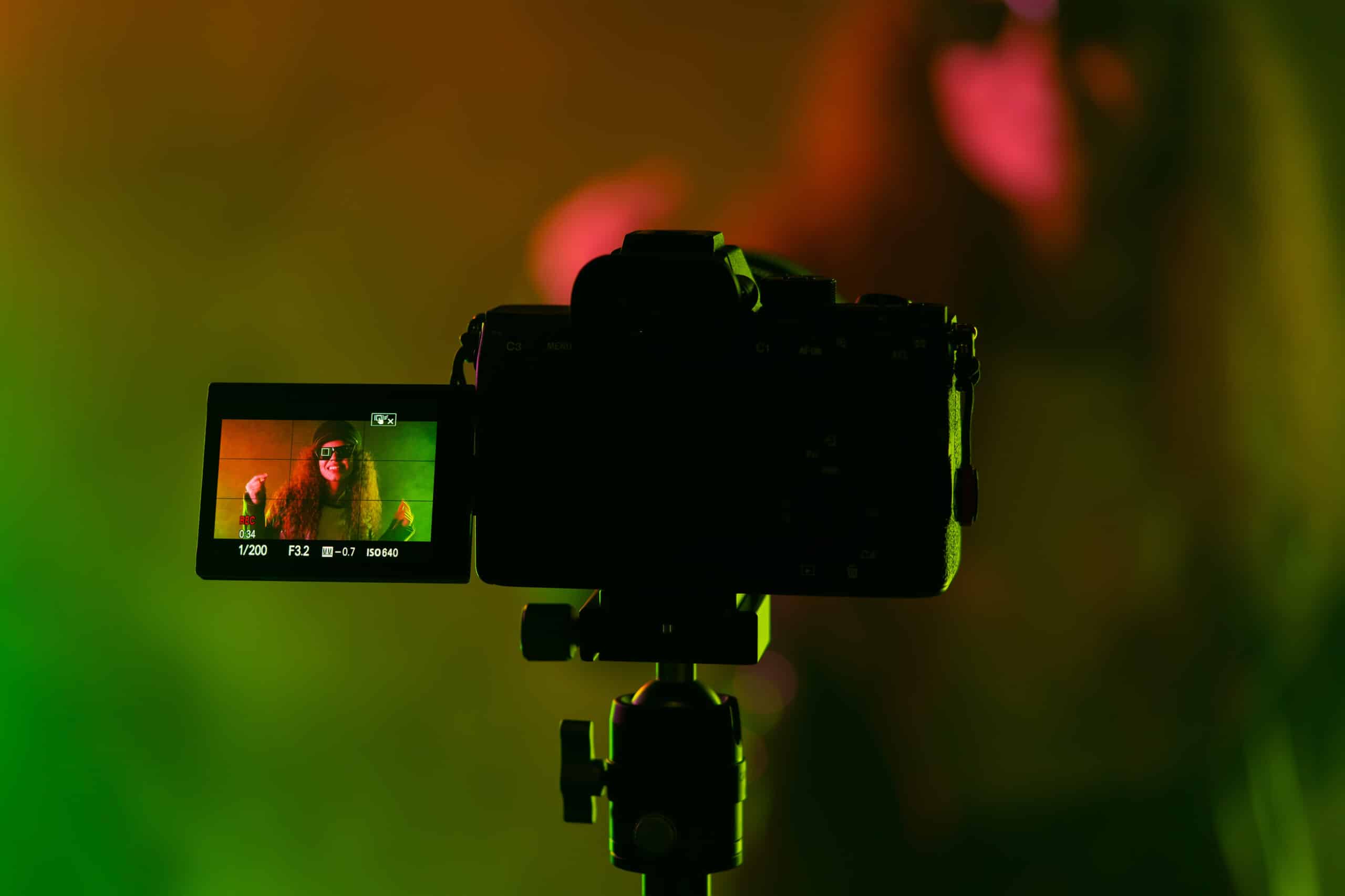 Backstage how operator working with professional camera. Videographer shoots music clip with actress or singer celebrity woman in dark studio with neon color light. High quality photo